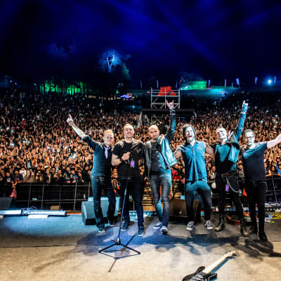 Ett rockband på scenen med publikhav i bakgrunden.