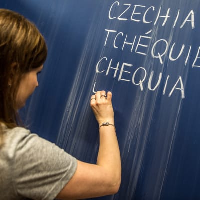 Tjeckisk lärare skriver de föreslagna nya kortformerna på engelska, franska och spanska för Tjeckien.