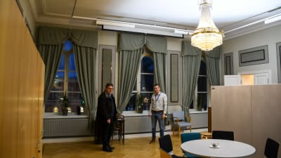 Två män i en stor sal med takkrona som gjorts om till kontorsrum.
