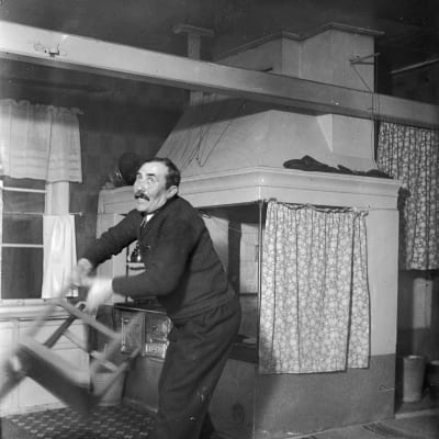 En man lyfter en stol med sin ena hand. Bilden är tagen 1938 i Närpes, Näsby.