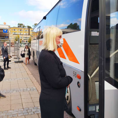 Kvinna bär vitt ansiktsskydd vid en buss med öppen dörr.