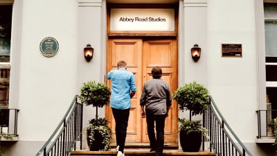 Kaj Korkea-aho och Kjell Westö går med ryggen vänd mot kameran upp för trappan till Abbey studios dörr. Ovanför dörren står det Abbey Road  Studios".