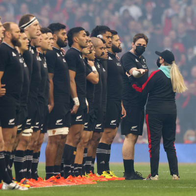 Uuden-Seelannin rugbymaajoukkue rivissä kuuntelemassa kansallislaulua. Rivin viimeisenä seisoo ylimääräinen henkilö, jota ollaan poistamassa kentältä.