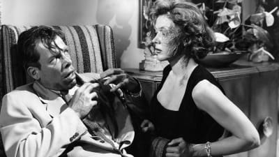 Järkyttyneen näköinen mies (Lee Marvin) katsoo naista, jonka kasvoista toinen puoli on arpeutunut (Gloria Grahame). Kuva elokuvasta Gangsterikuningas (The Big Heat, 1953).