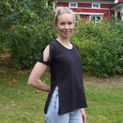 En kvinna som står i en trädgård framför ett rött hus.