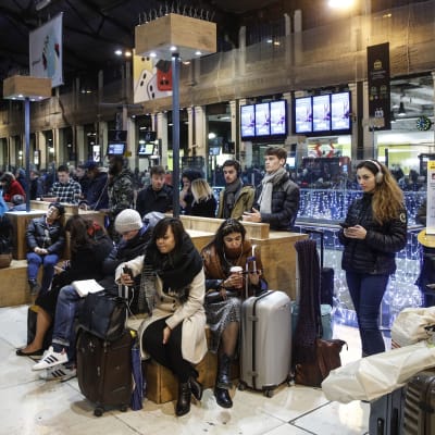 Massvis med människor sitter och väntar på sina tåg i en tågstation.