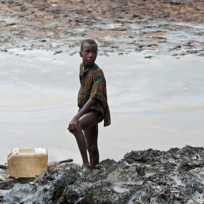 En nigeriansk pojke med ett fiskenät vid en flodbank dränkt i olja.
