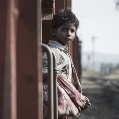 Saroo (Sunny Pawar) står på trappsteget till ett tåg och ser rakt in i kameran.