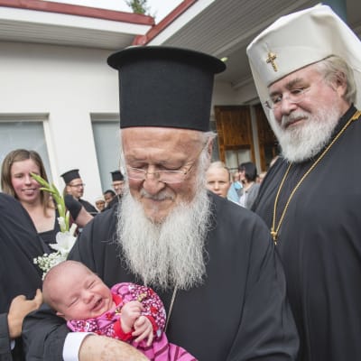 Ärkebiskop Leo ser på medan patriark Bartolomeos I håller en nyfödd baby i famnen.