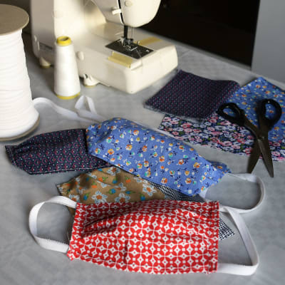 Munskydd av tyg i olika färger och mönster ligger på ett bord bredvid en symaskin.