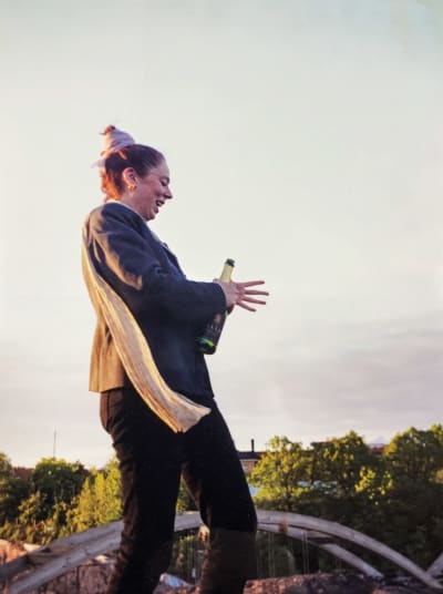 En kvinna står på en klippa i solnedgång med en öppnad skumvinsflaska.