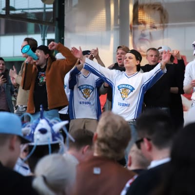 Jääkiekon MM-kullan juhlijoita Porin torilla, Leijona-paitaan pukeutunut nuori mies huudattaa kansaa.