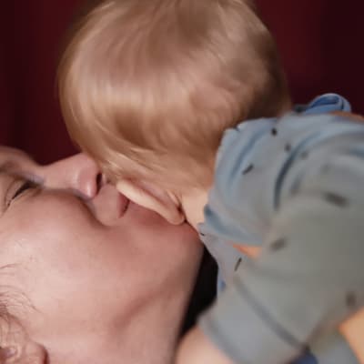 Soiva syli: äiti suukottaa lasta poskelle