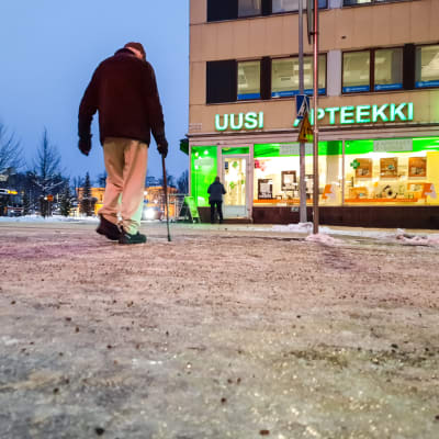 Äldre man går över gatan i Borgå centrum. Bilden är tagen nerifrån och man ser is, snö och sand på marken.