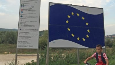 Två skyltar, den ena med EU:s flagga på, i förgrunden en pojke på cykel. Taget i Kroatien.