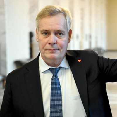 Antti Rinne tittar in i kameran och ler smått. Han lutar med ena armen mot ett dörrhandtag i riksdagen den 14.12.2020.