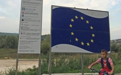 Två skyltar, den ena med EU:s flagga på, i förgrunden en pojke på cykel. Taget i Kroatien.
