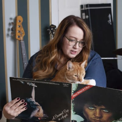 Jutta Carpelan sitter med sin katt i famnen och tittar på en vinylskiva.