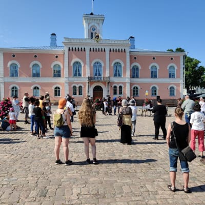 Flera personer står i solskenet på Lovisa torg.