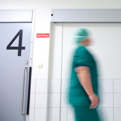 En sjukskötare går förbi två dörrar på ett sjukhus.