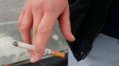 En hand som håller i en cigarett mellan pek- och långfingret.