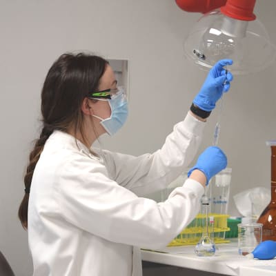 En kvinnlig kemist håller upp instrument i AstraZenecas laboratorium i Sydney där man jobbar med att ta fram ett coronavaccin.