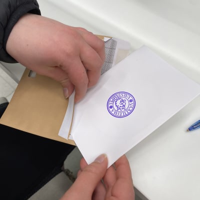 Närbild på händer som sätter en röstningssedel i ett kuvert.