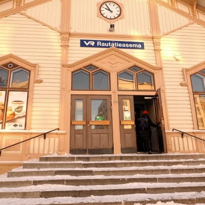 Oulun puisen rautatieaseman sisäänkäynti, ja matkustaja menossa sisään taloon.