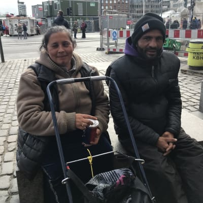 En man och en kvinna sitter på ett stenblock på ett torg i Köpenhamn.