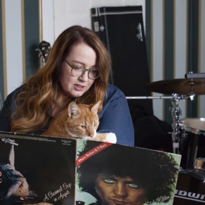 Jutta Carpelan sitter med sin katt i famnen och tittar på en vinylskiva.