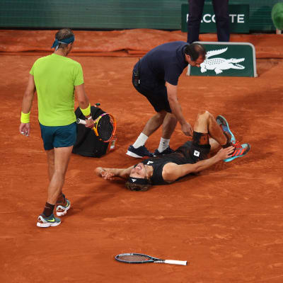 Alexander Zverev ligger på planen efter sin skada. Rafael Nadal kommer för att kolla läget.