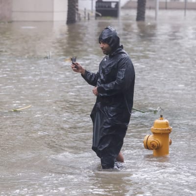 En man står och vadar i knähögt vatten på en gata i Miami.