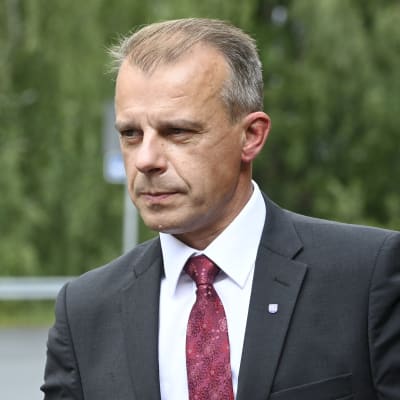 Centerns gruppordförande Juha Pylväs iklädd kostym och vinröd slips. i bakgrunden gröna lummiga träd.