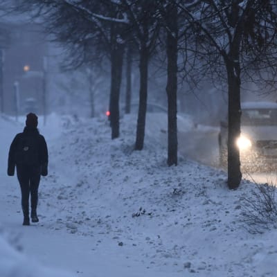 Jalankulkija ja autoliikennettä lumipyryssä.