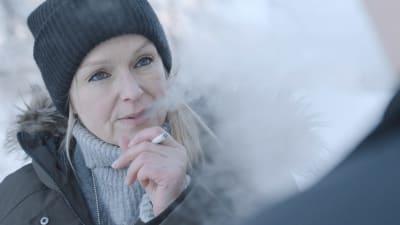 Anu Sinisalo i rollen som Lena Jaakkola i serien Sorjonen. Pipo och cigarrett i handen, snö bakom.