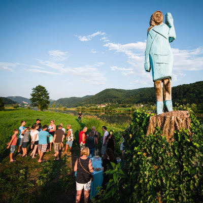 En staty i trä av Melania Trump. Människor står och tittar på statyn.