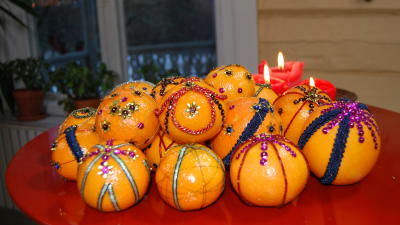 Eb röd bricka med mandariner och apelsiner som dekorerats med paljetter och sidenband i olika färger.