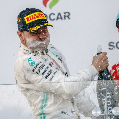 Sebastian Vettel skrattar åt Valtteri Bottas med champagne runt munnen och en flaska i handen.
