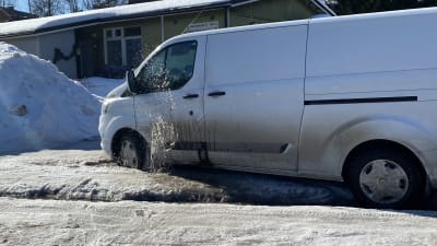 En paketbil har fastnat i gropar på en snöig väg. Framhjulet sprättar upp vatten.