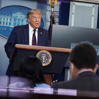 President Donald Trump står vid ett podie framför journalister i Vita huset.