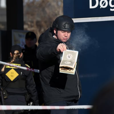 Rasmus Paludan polttaa koraania kädessään kadulla. Edessään ja takanaan huomionauhaa ja poliiseja.
