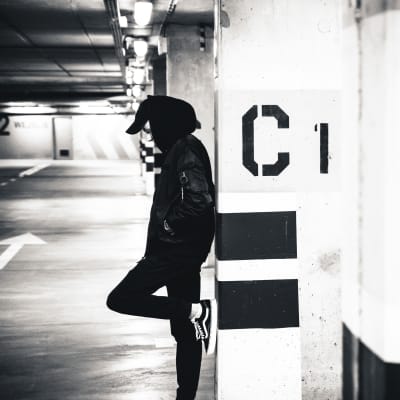 Ung man står i ett parkeringsgarage lutar sig mot en betongstolpe.