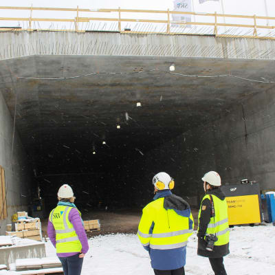 Tre personer står i mynningen till tunneln som är under byggnad, det snöar