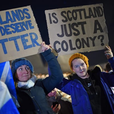 kaksi mielenosoittajaa pitää kylttejä joissa toivotaan skotlannin itsenäistymistä