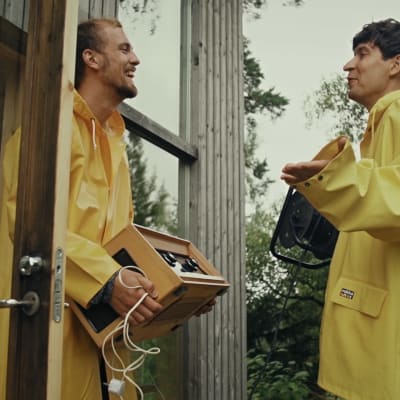 Kasper och Jussi Virta i gula regnrockar vid dörren till en stuga