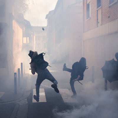 Demonstranter kastar sten i ett moln av tårgas.