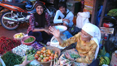 Kvinnor i Malaysia på en marknad. Kvinnorna sitter vid fruktskålar.