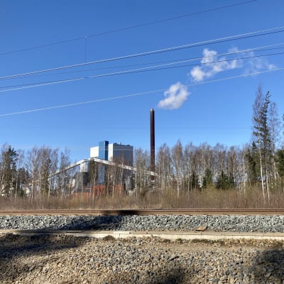 Junaradan takana näkyy voimalaitos, jonka piipusta tulee savua.