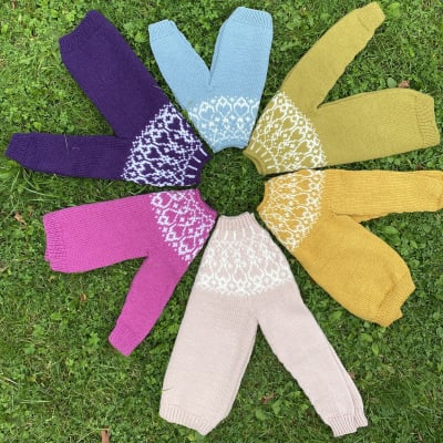 Sex stickade barntröjor i olika färger ligger i en ring på gräsmattan.