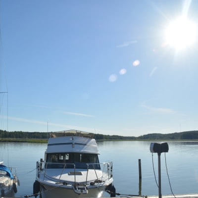 Båtar står förtöjda vid en kaj. Havet ligger platt och solen skiner.